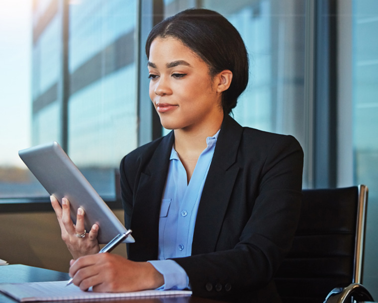 woman reviewing data on a tablet while making notes