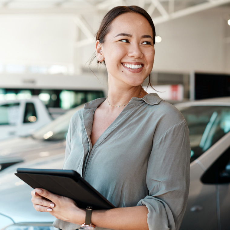 smiling woman with tablet in front of cars