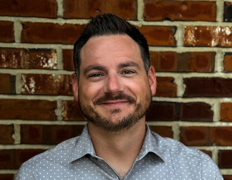 Corey Nolan, Software Training Specialist, smiling in front of a brick wall